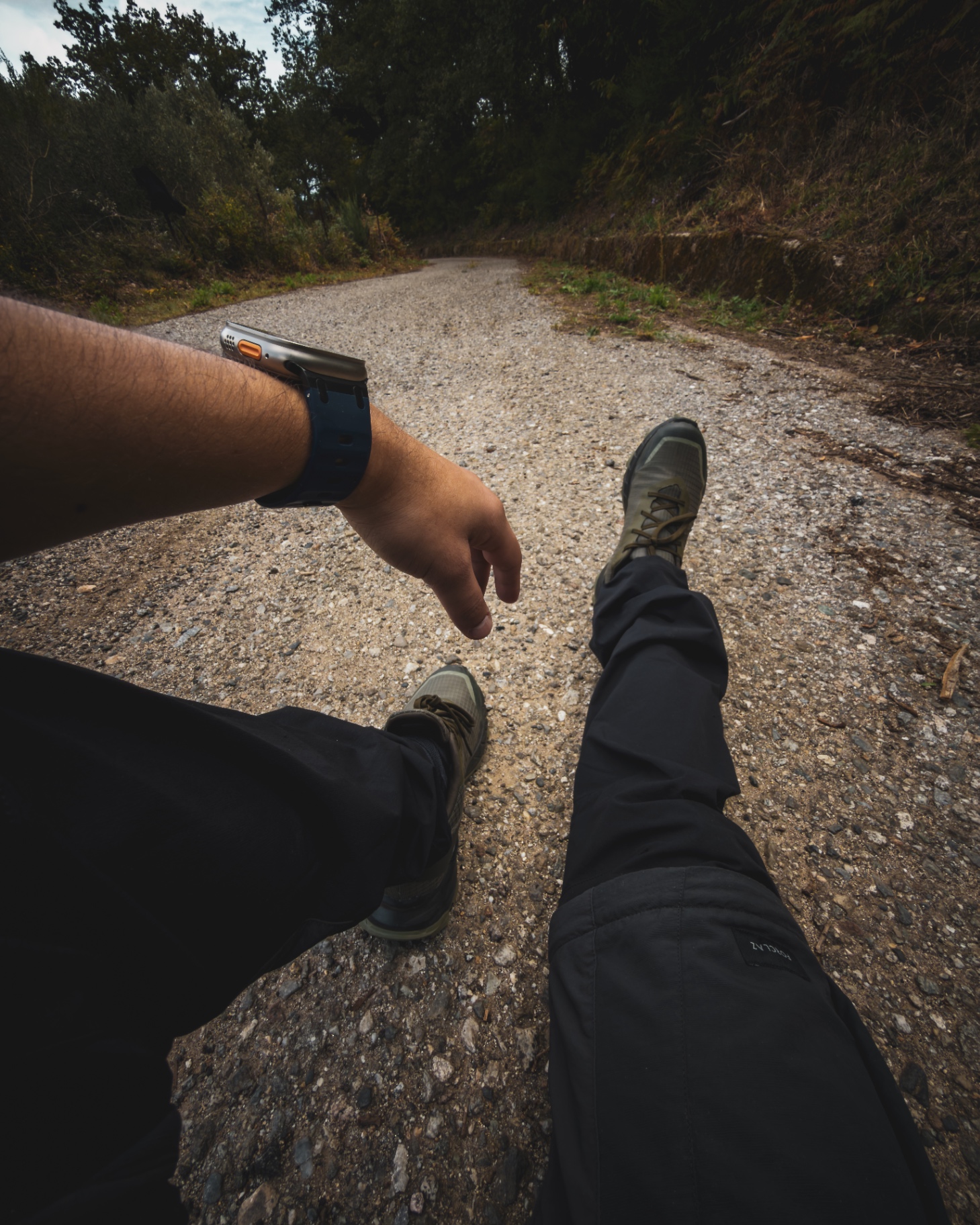 Pausa sul sentiero sterrato: gambe distese, scarpe da trekking e watch sul polso